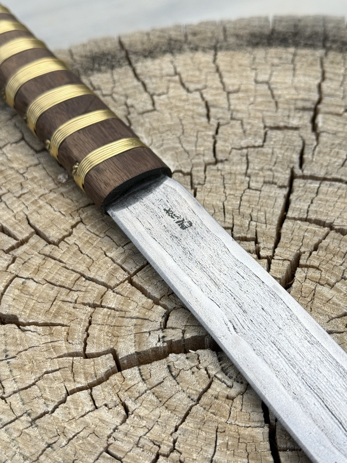 Close view of the etched composite blade meeting the brass wire-wrapped wooden handle