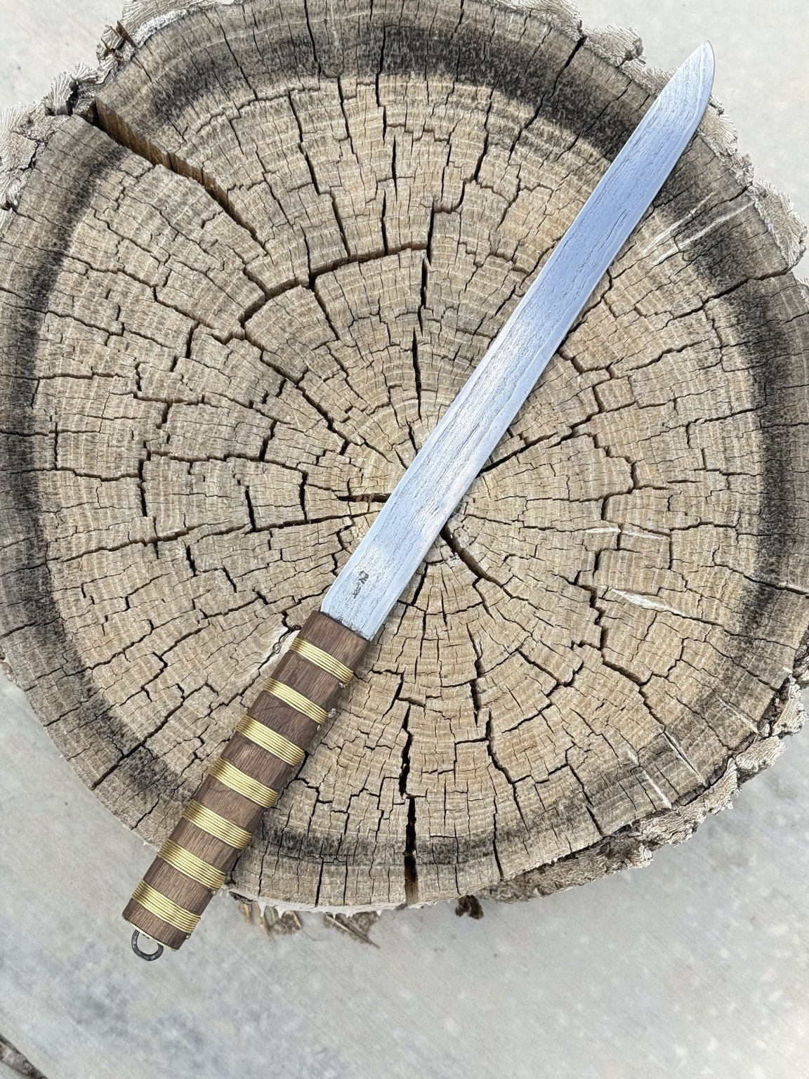 Finished Viking Age Scandinavian long knife with a brass wire-wrapped oak grip, displayed on a weathered stump